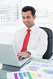 Smiling young businessman with laptop and graphs