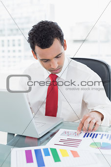 Businessman with laptop working on graphs at desk