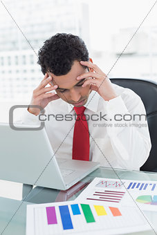 Serious businessman with laptop and graphs at desk