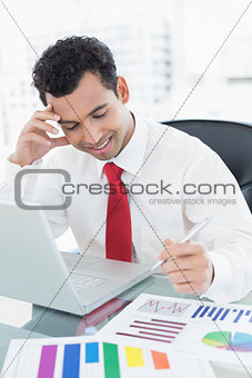 Smiling young businessman with laptop and graphs