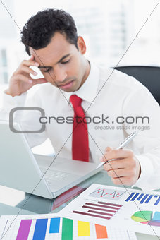 Serious businessman with laptop and graphs at office