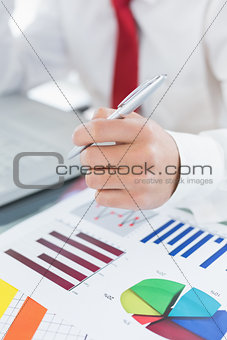 Mid section of a businessman with laptop and graphs at desk