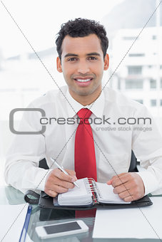 Smiling businessman writing in diary at office
