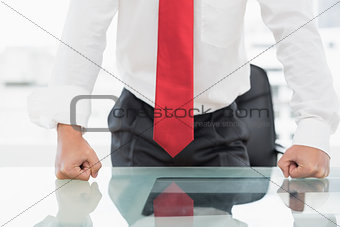 Mid section of a businessman with clenched fists on desk