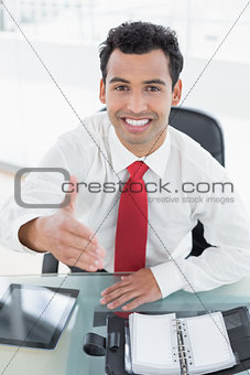 Businessman offering a handshake at office desk