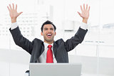 Businessman cheering in front of laptop at office desk