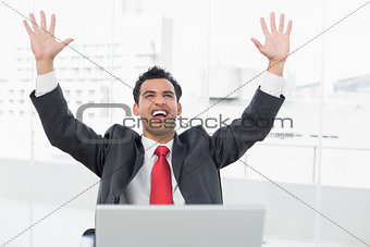 Businessman cheering in front of laptop at office desk