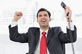 Businessman cheering with telephone receiver at office