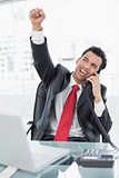 Businessman cheering while on call at office desk