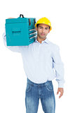 Serious handyman in hard hat carrying a toolbox