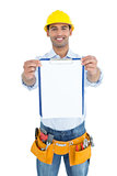 Smiling handyman in yellow hard hat holding clipboard
