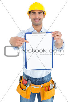 Smiling handyman in yellow hard hat pointing at clipboard