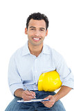 Smiling handyman with yellow hard hat writing in clipboard