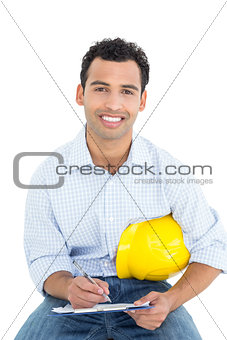 Smiling handyman with yellow hard hat writing in clipboard