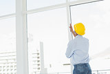 Handyman in yellow hard hat examining window in office