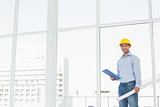 Handyman in hard hat with clipboard and blueprint in office