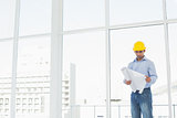 Architect in yellow hard hat looking at plans in office