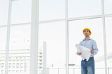 Young architect in yellow hard hat with plans in office