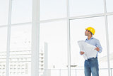 Architect in yellow hard hat with plans looking up at window