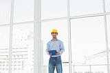 Young architect in yellow hard hat with clipboard in office