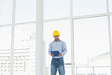Smiling architect in yellow hard hat with clipboard in office
