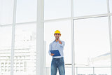 Architect in hard hat with clipboard gesturing thumbs up in office