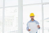 Architect in yellow hard hat looking at blueprint in office