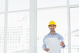 Smiling architect in yellow hard hat with blueprint in office