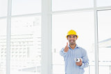 Architect in hard hat with blueprint gesturing thumbs up in office