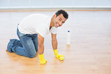Smiling young man cleaning the parquet floor at house