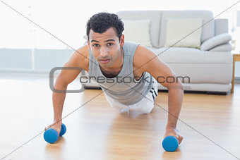 Sporty man with dumbbells doing push ups in the living room