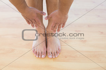 Man stretching hands towards his feet on parquet floor