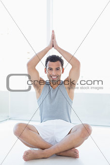 Smiling young man sitting with joined hands over head