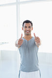 Fit young man gesturing thumbs up in fitness studio