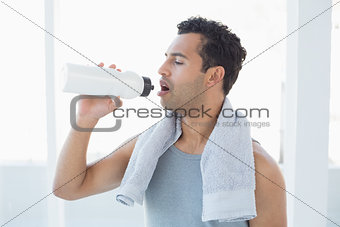 Man with towel around neck drinking water in fitness studio