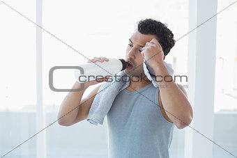 Man drinking water while wiping sweat with towel in fitness studio