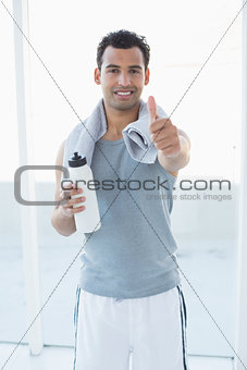 Man with water bottle and towel gesturing thumbs up in fitness studio