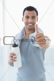 Man with water bottle and towel gesturing thumbs up in fitness studio