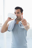 Man drinking water while gesturing thumbs up in fitness studio