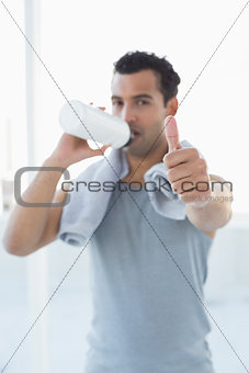 Man drinking water while gesturing thumbs up in fitness studio