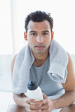 Man with towel around neck holding water bottle in fitness studio