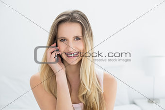 Beautiful smiling young woman using cellphone in bed
