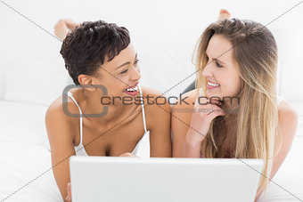 Happy female friends using laptop in bed