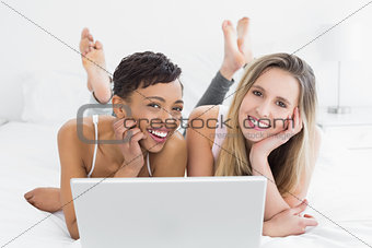 Relaxed young female friends using laptop in bed