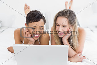 Happy relaxed friends using laptop in bed