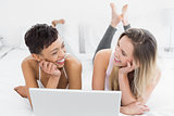 Cheerful female friends using laptop in bed