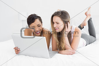 Cheerful relaxed female friends using laptop in bed