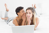 Relaxed female friends with laptop gossiping in bed