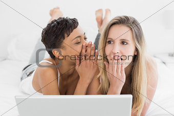 Female friends with laptop gossiping in bed