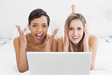 Shocked young female friends with laptop in bed